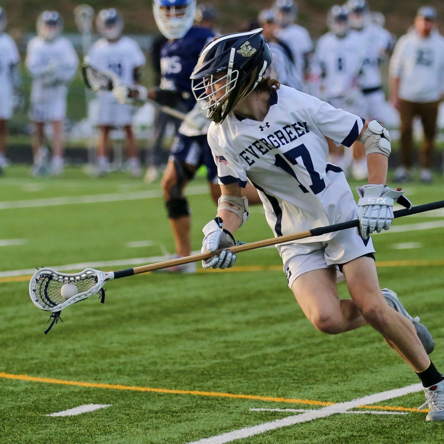 Person playing lacrosse on a field with teammates and opponents in the background